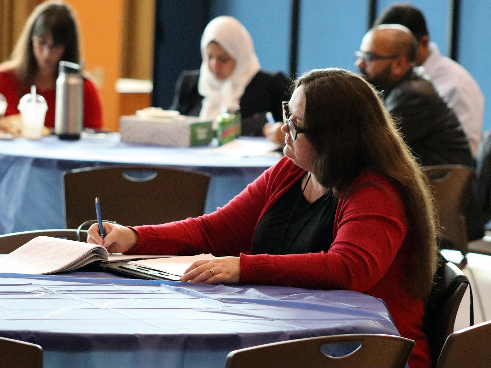 A student sitting at a table writes on a notepad