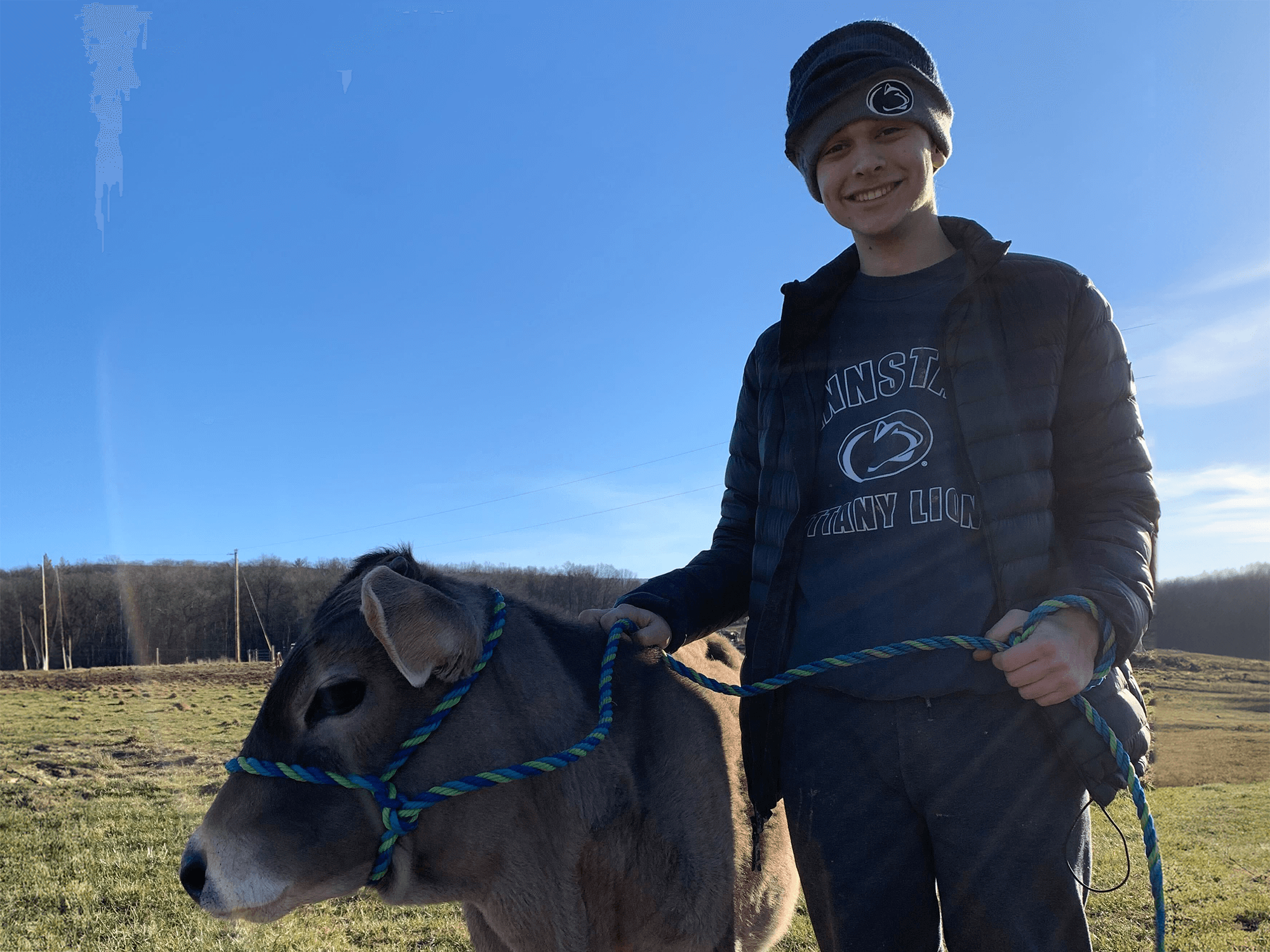 Ethan Sten stands to the right of a cow, holding its harness in a field at Gita Nagari Eco Farm and Sanctuary in Port Royal, Pennsylvania.