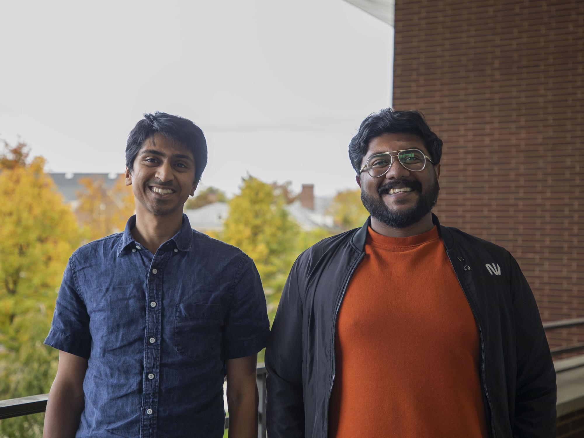 two smiling people, brick wall and green trees in background