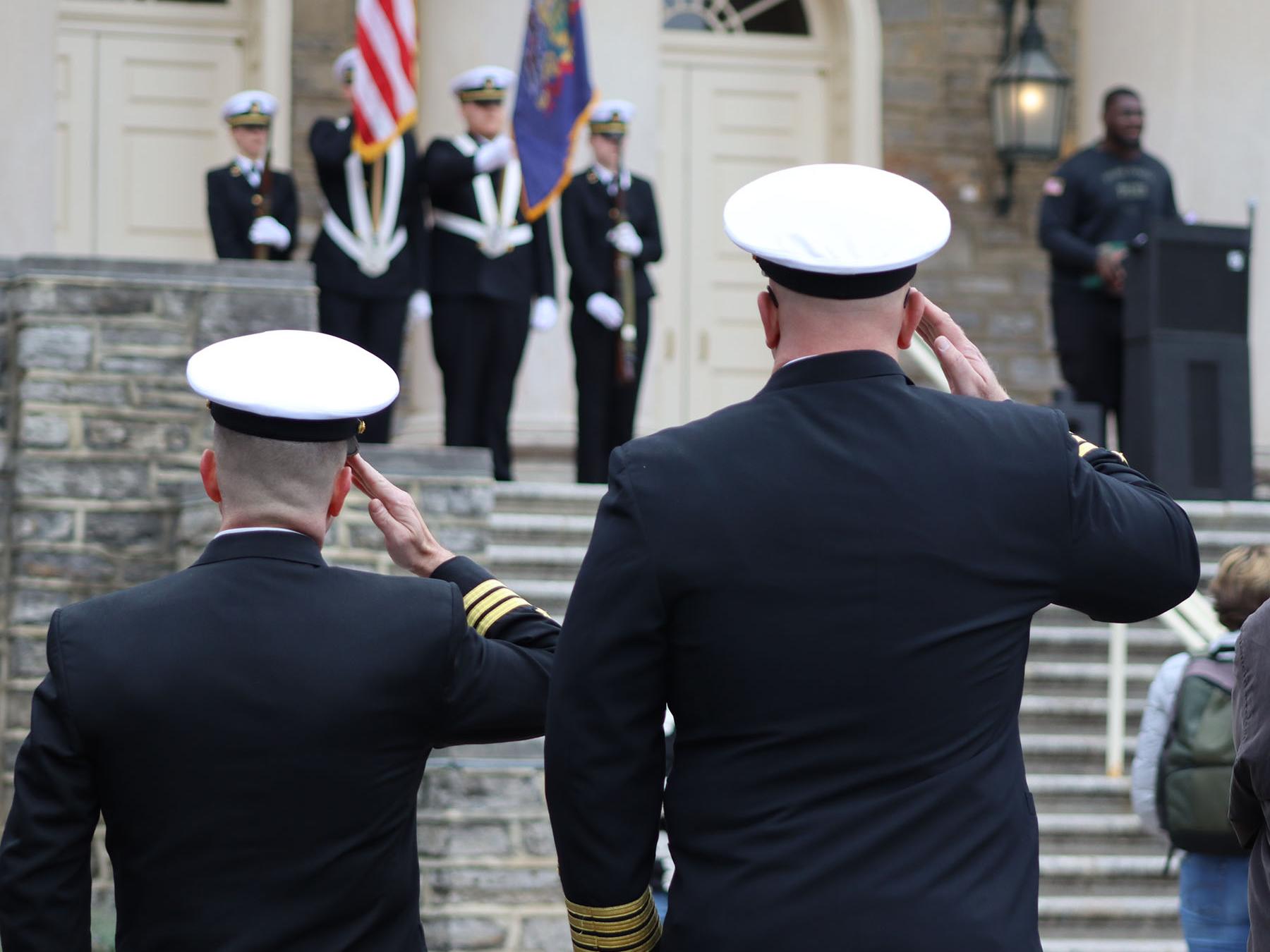 Two people wearing military uniforms salute the American Flag.