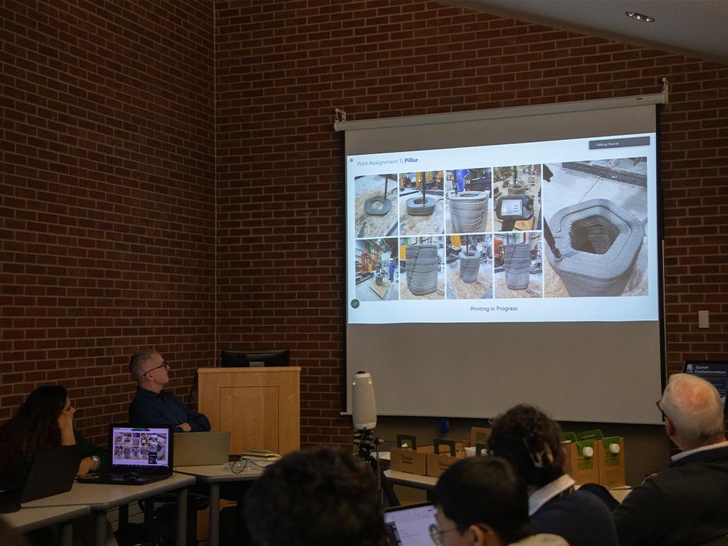 Faculty and reviewers view 3D printed concrete structures that are projected on a screen. 