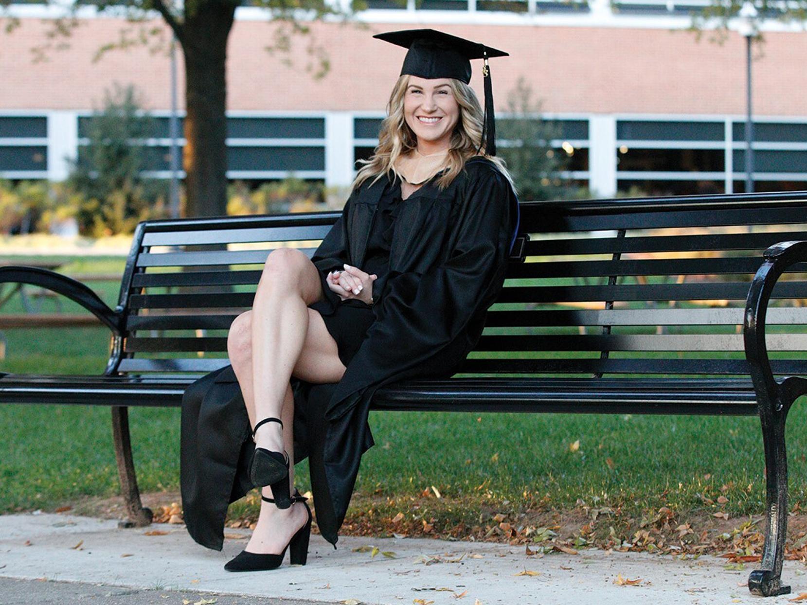 Kylee Altland in graduation regalia sitting on bench