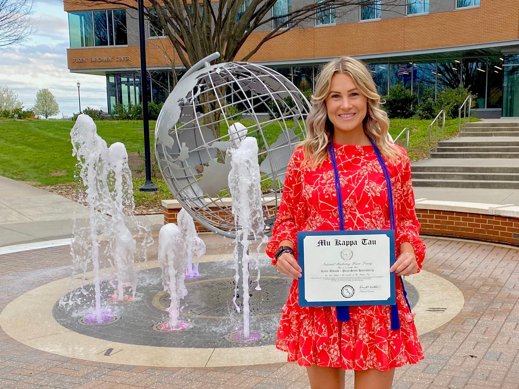 Kylee Altland in from of globe fountain holding certificate