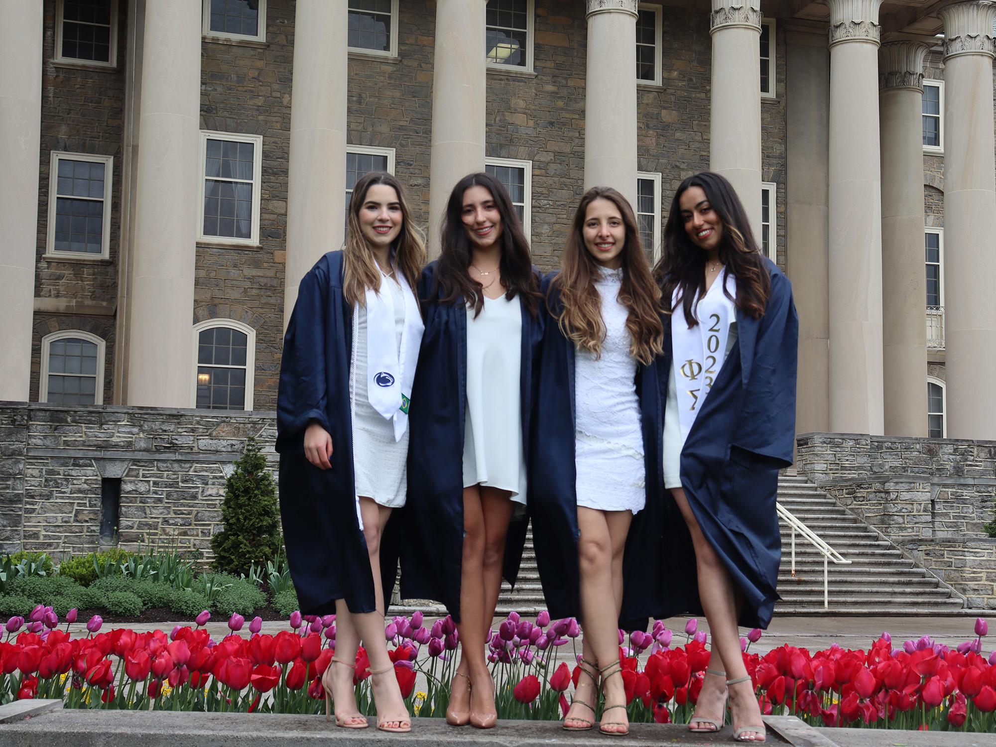 Nina Castillo Schoonewolff, second from the left, and her friends pose for graduation photos in front of Old Main at Penn State University Park.