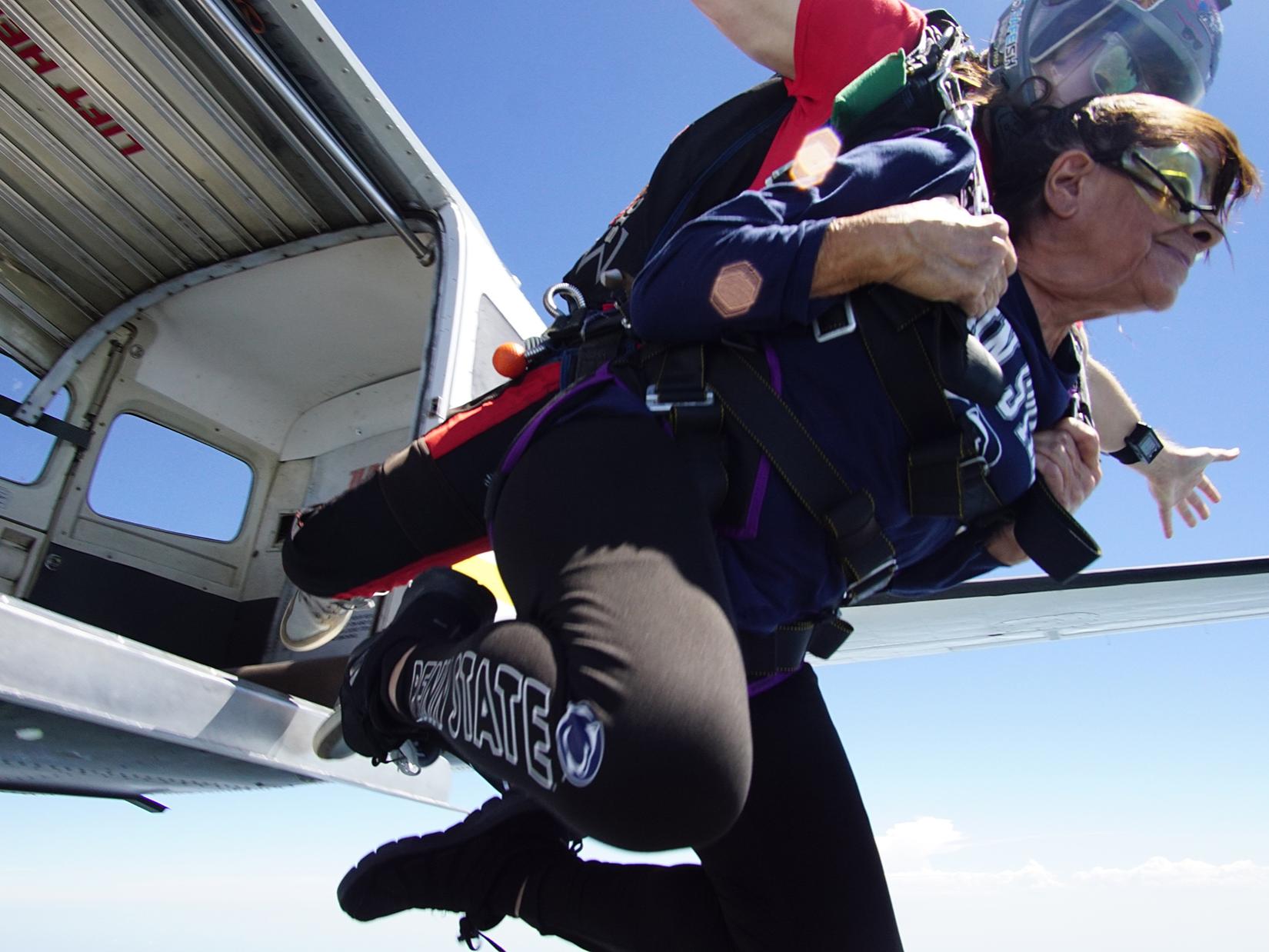 A woman wearing Penn State pants and shirt jumps out of an airplane