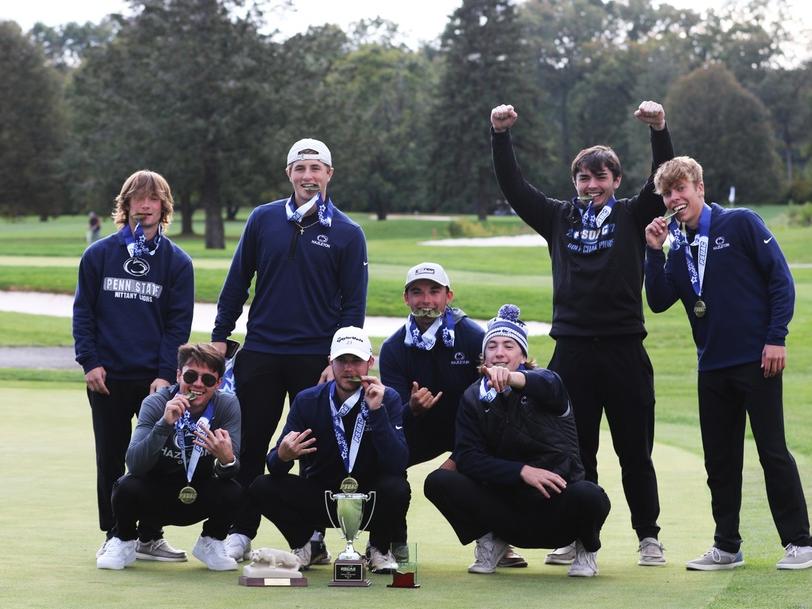 Group of eight students on a golf course holding golden medals and celebrating.
