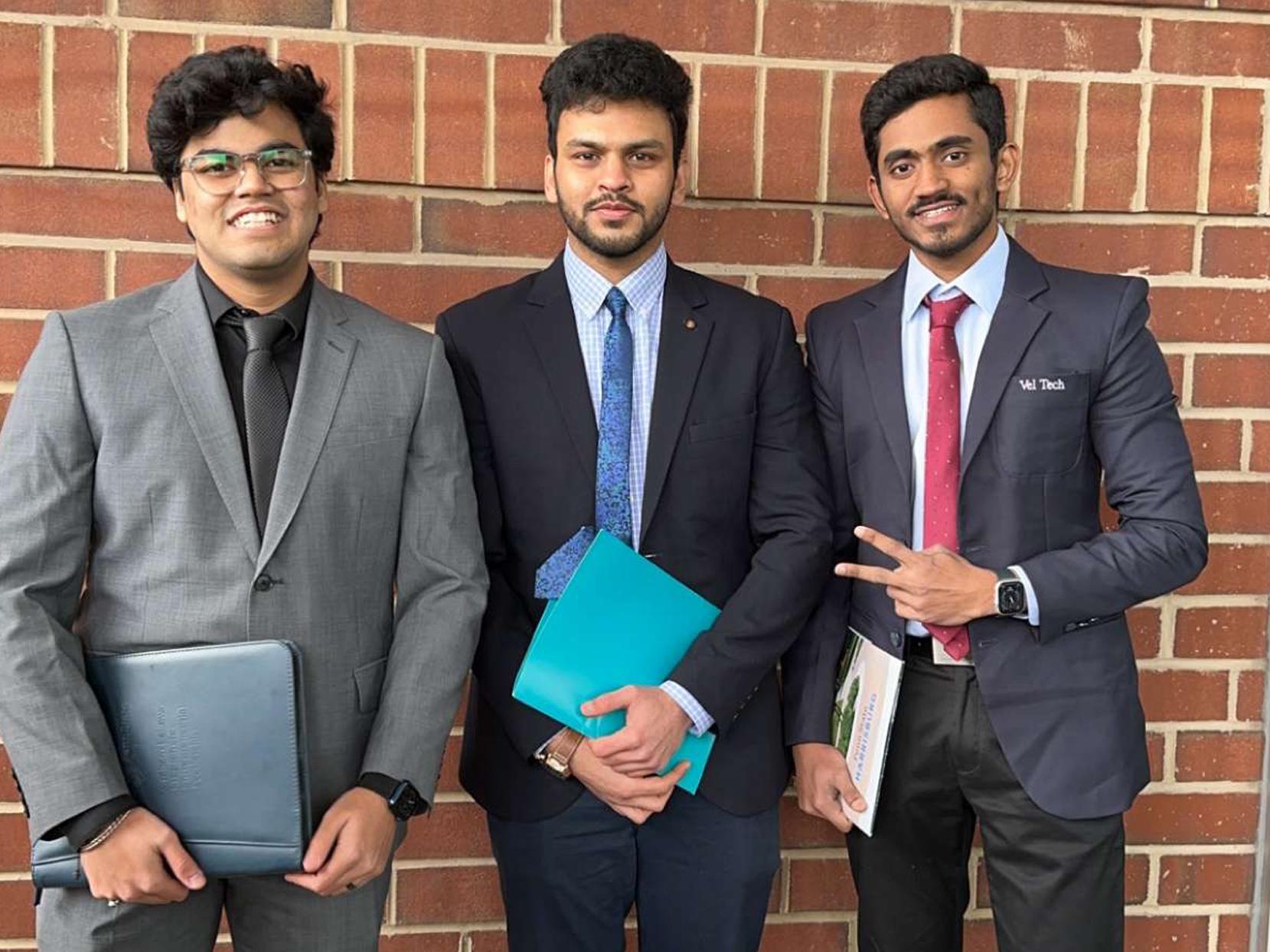 Purav and two friends all in suits holding folders