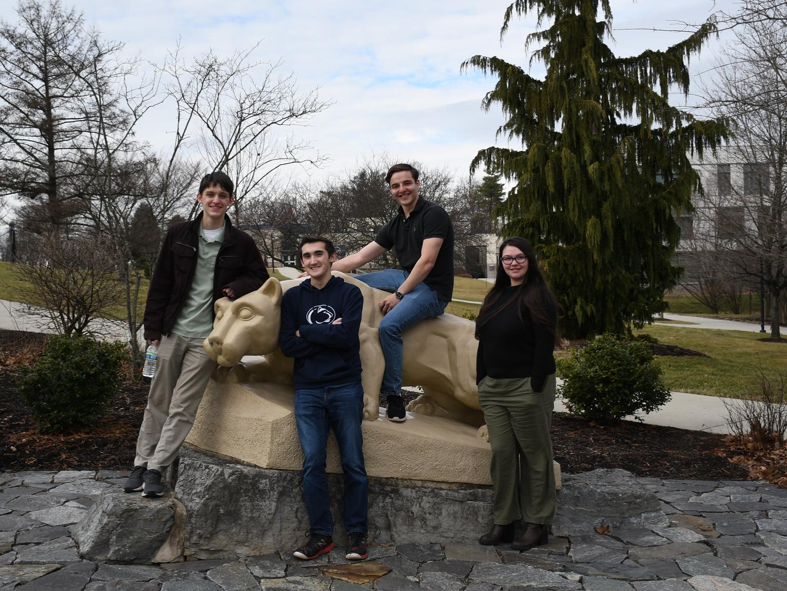 Four male students pose for picture on Nittany Lion statue