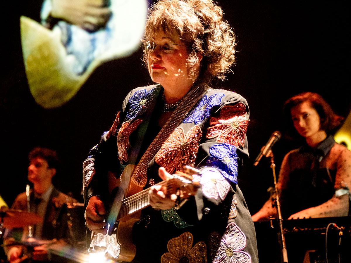 A woman plays guitar on a stage with a band.