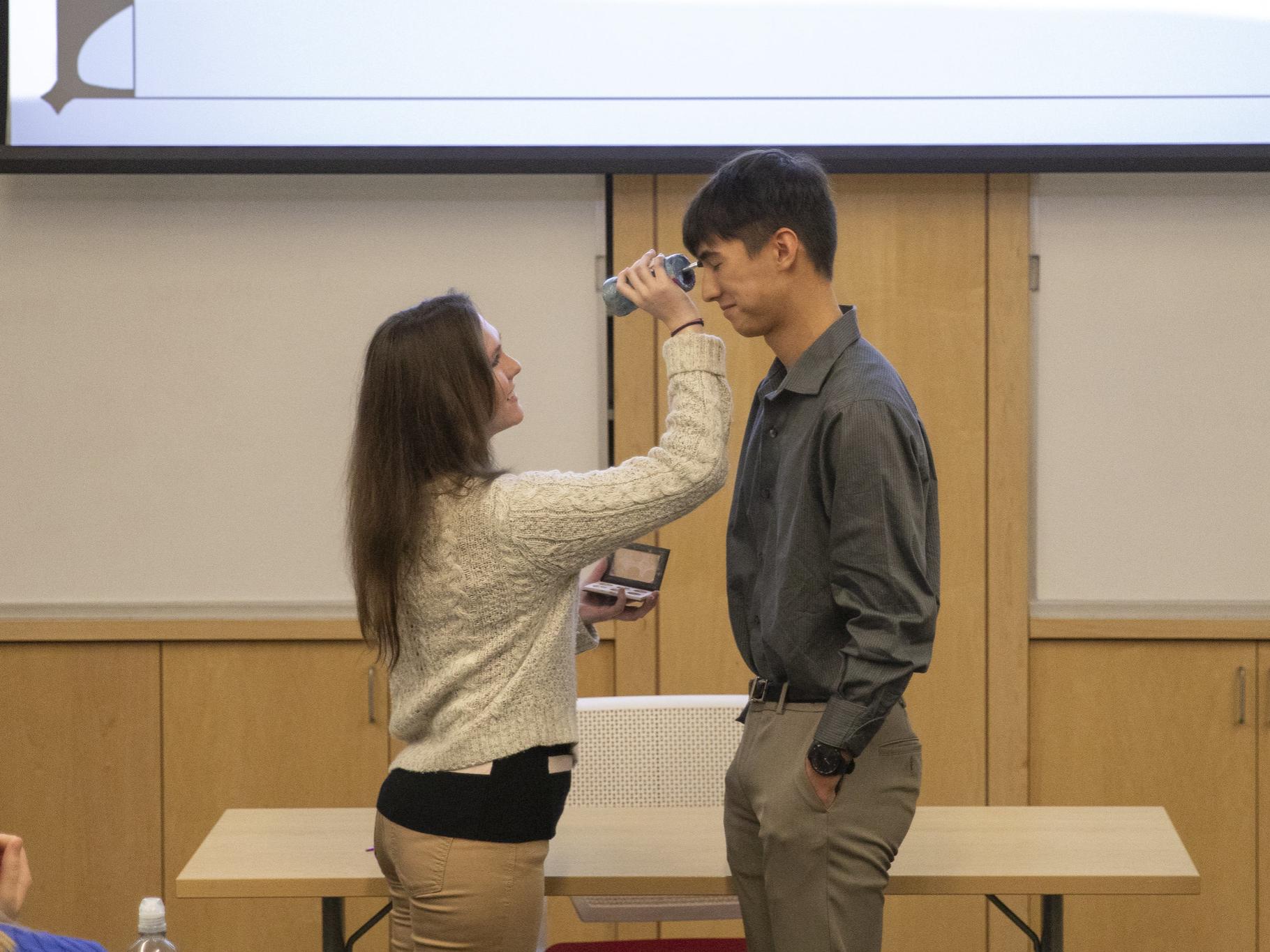 Female student presses makeup brush to male student's face