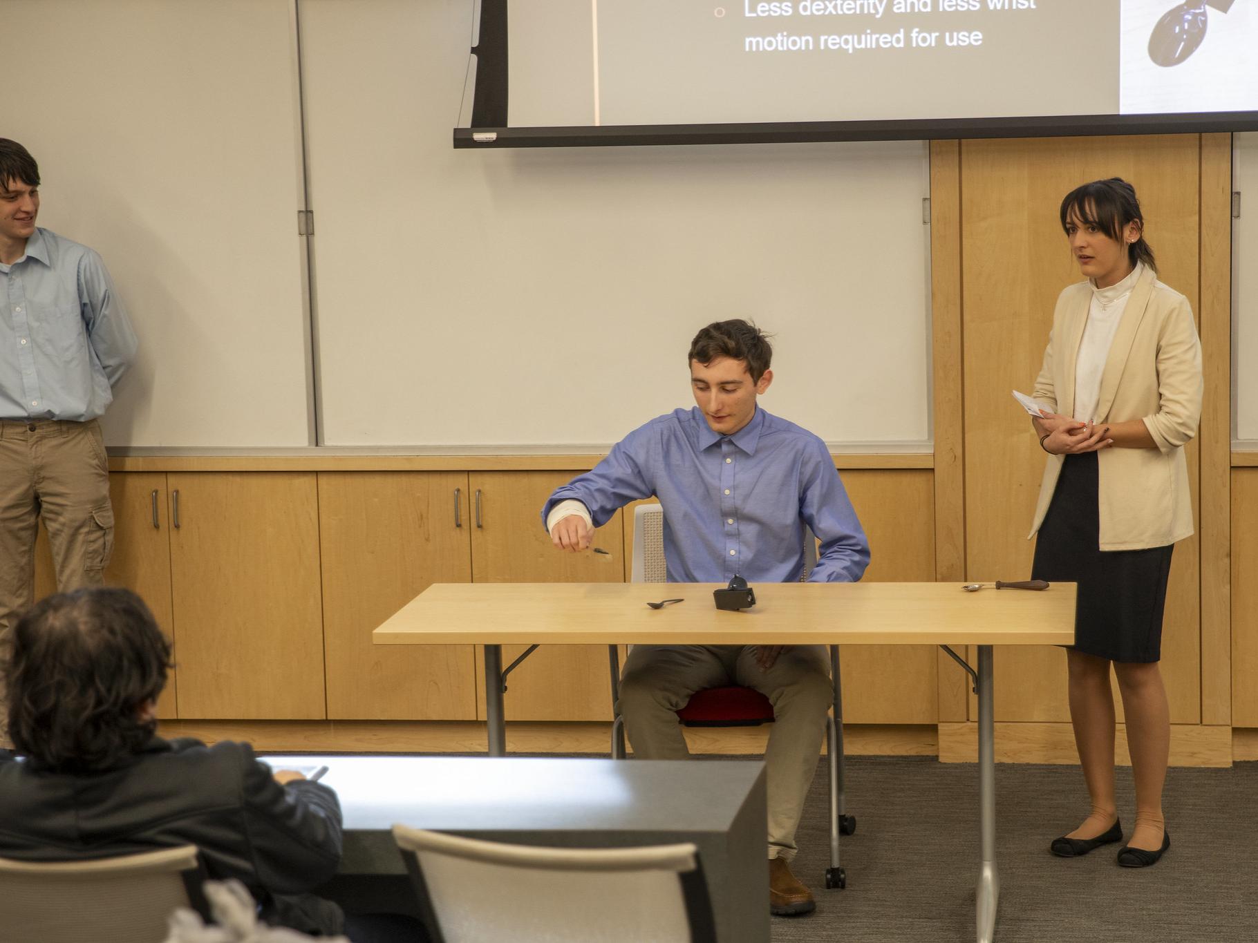 Three students present assistive utensil device to attendees