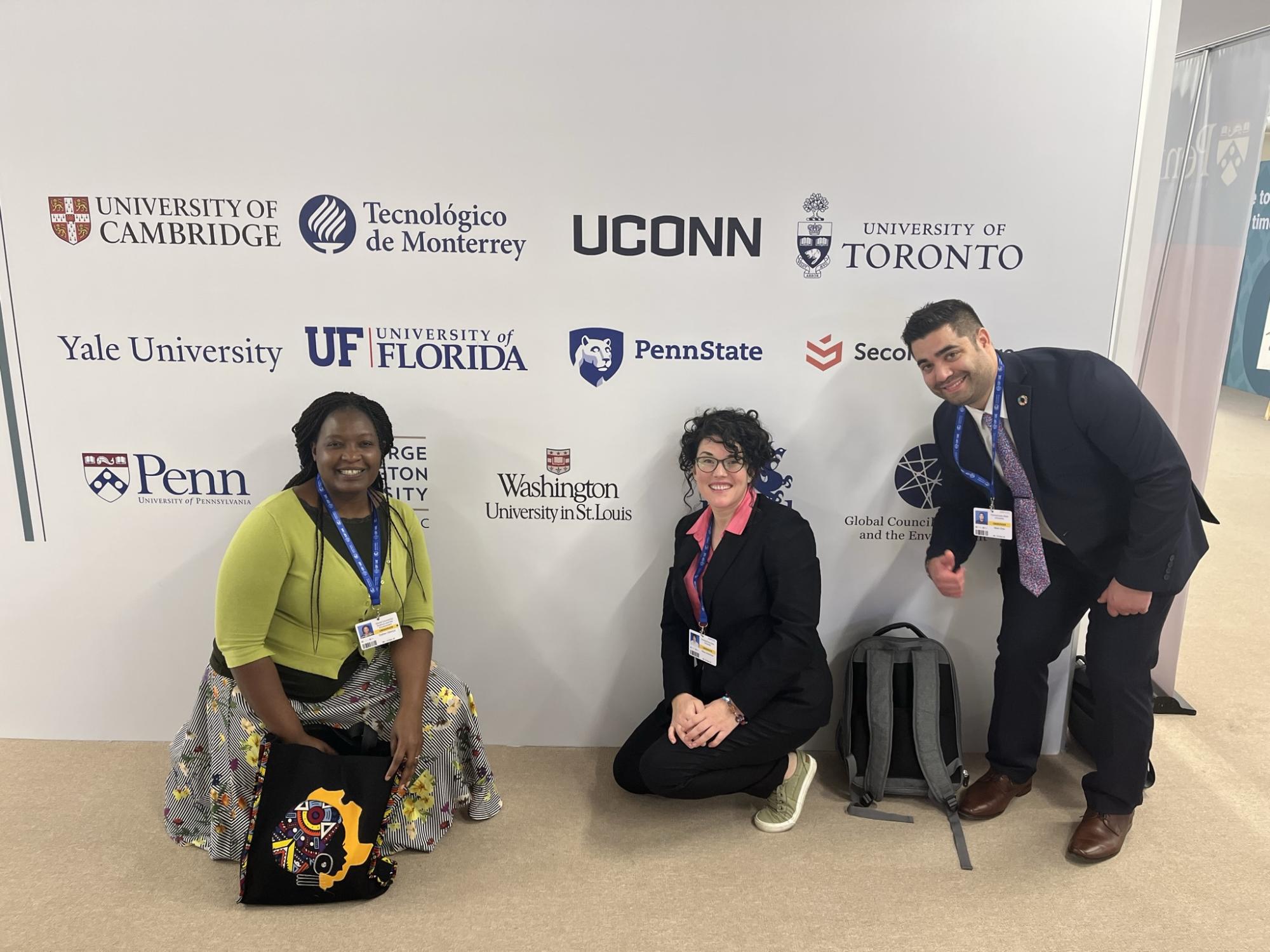 Olivia McMahon and two members of the Penn State delegation post for a photo in front of a banner with other universities' names on it