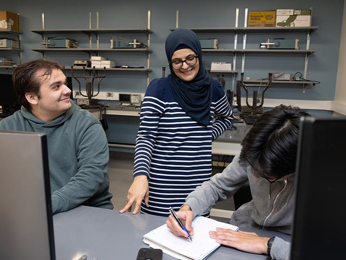 A professor works with two students in the classroom