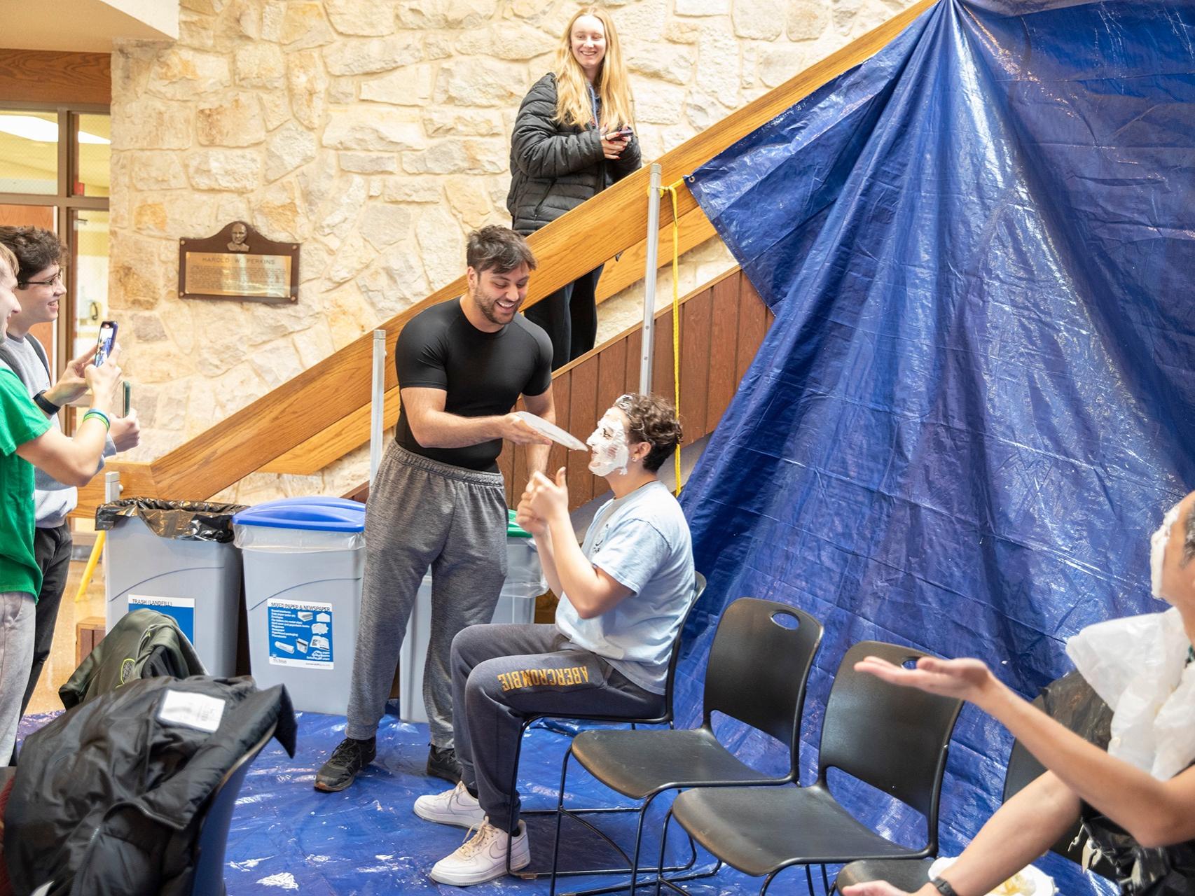 Male student pies another male student's face with whipped cream