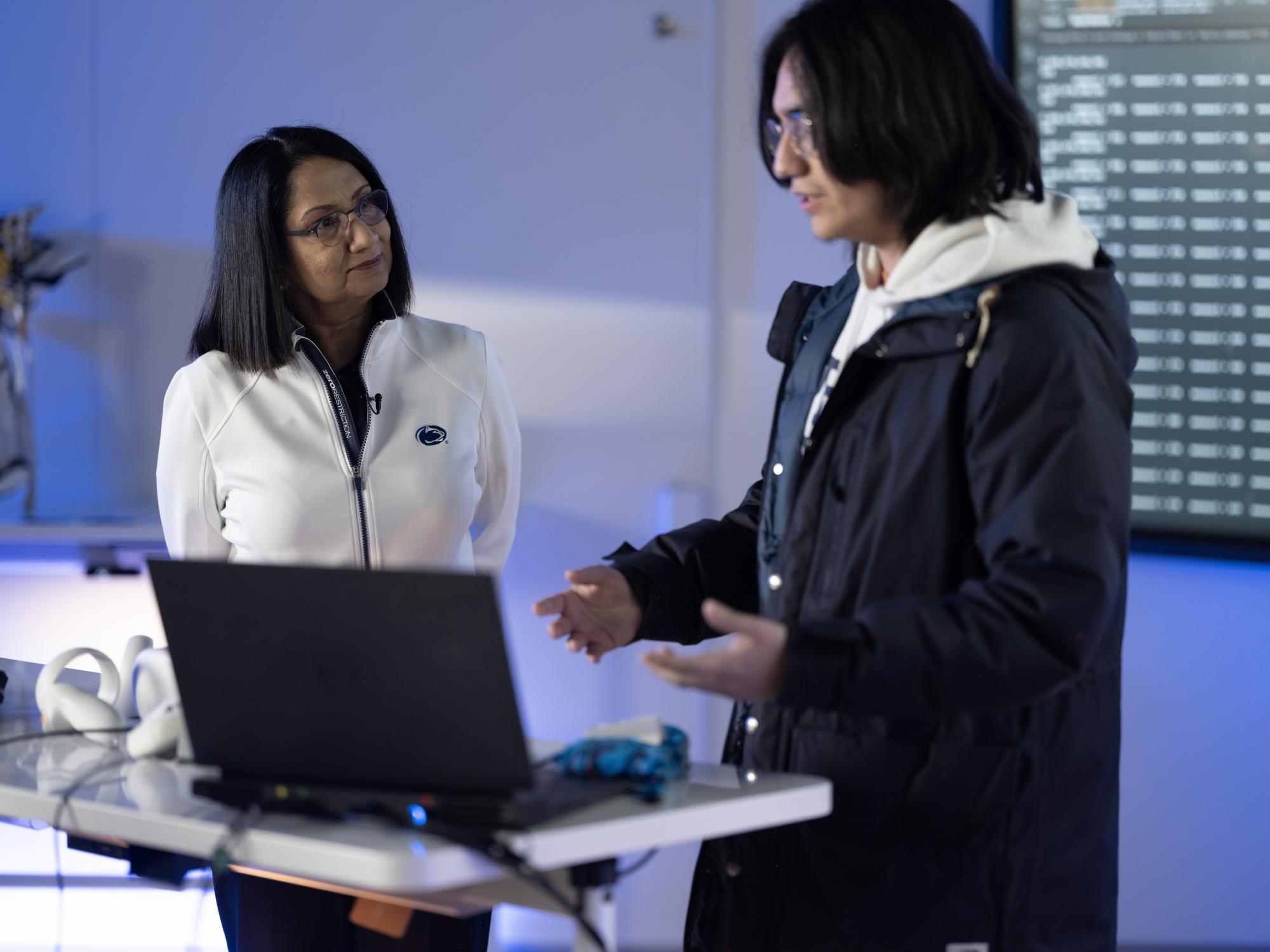 Neeli listens to Isaac as he explains his work in front of a laptop and the haptic glove.