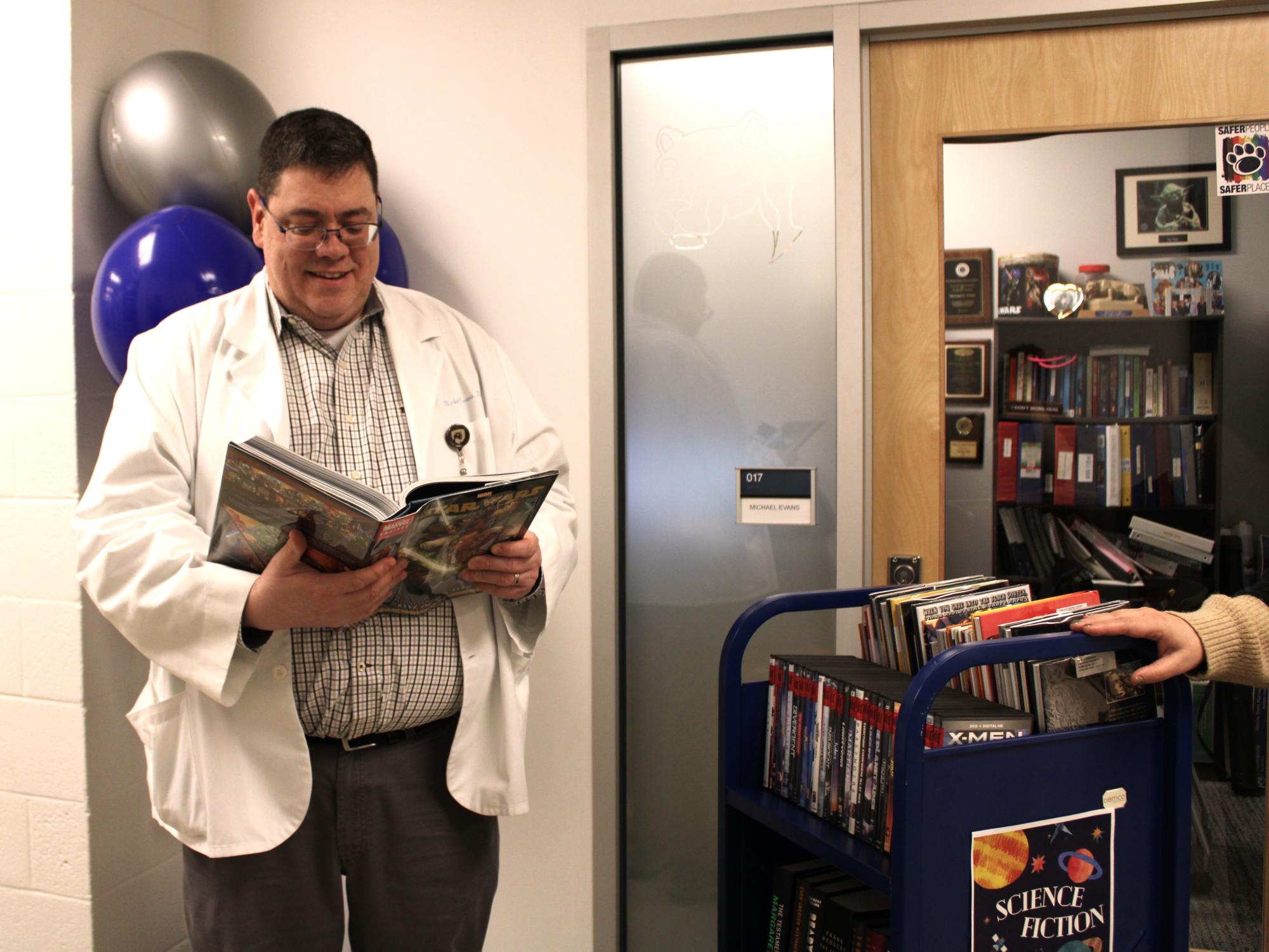 Nursing professor Mike Evans looks over a book on the Sci-Fi library cart