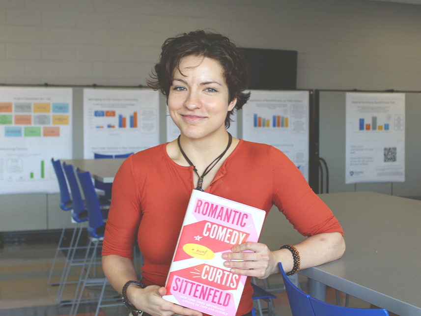 Student Jade Snyder smiling and posing with her chosen book "Romantic Comedy".