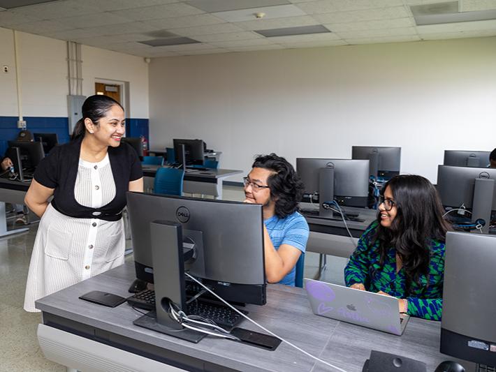 The professor stands to the left of the photo talking to two students who are seated to the right.Dr. Madhurima Ray, left, assistant professor of computer science at Penn State Beaver, interacts with Quang Nguyen, center, and Astha Kole, during class. Quang and Astha are both second-year computer science majors.  