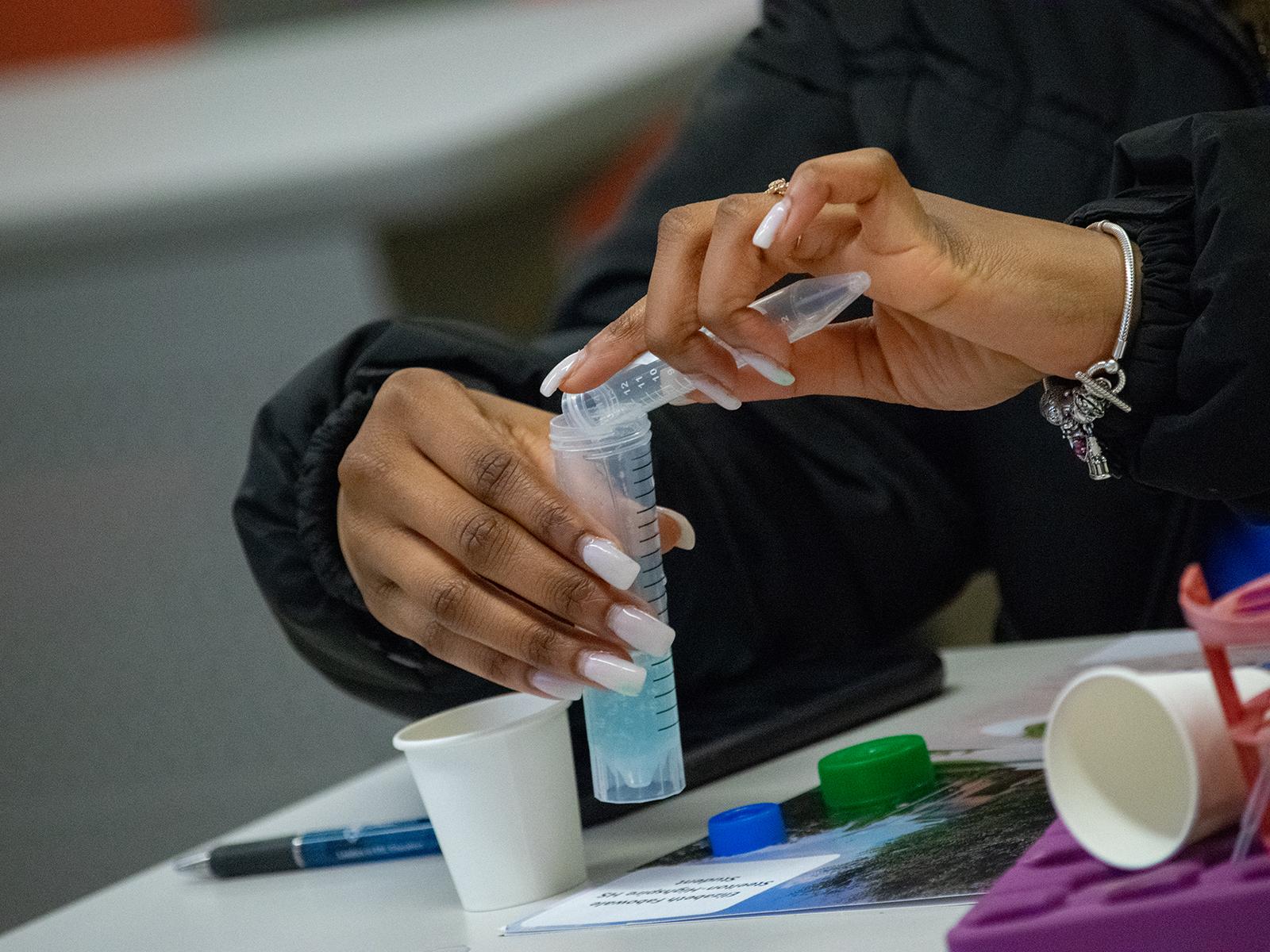 Closeup of a student's hands pouring liquid into a test tube