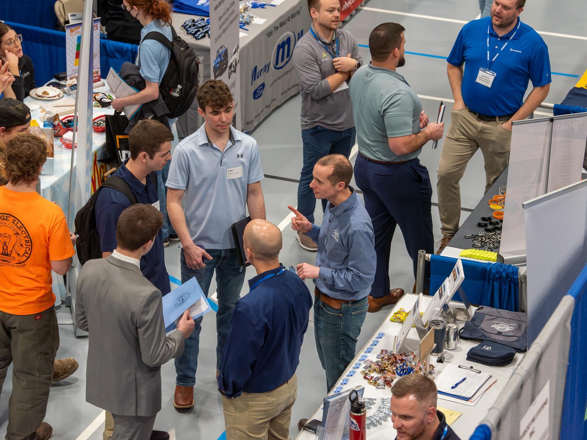 A group of people stand on the floor at a career fair. 