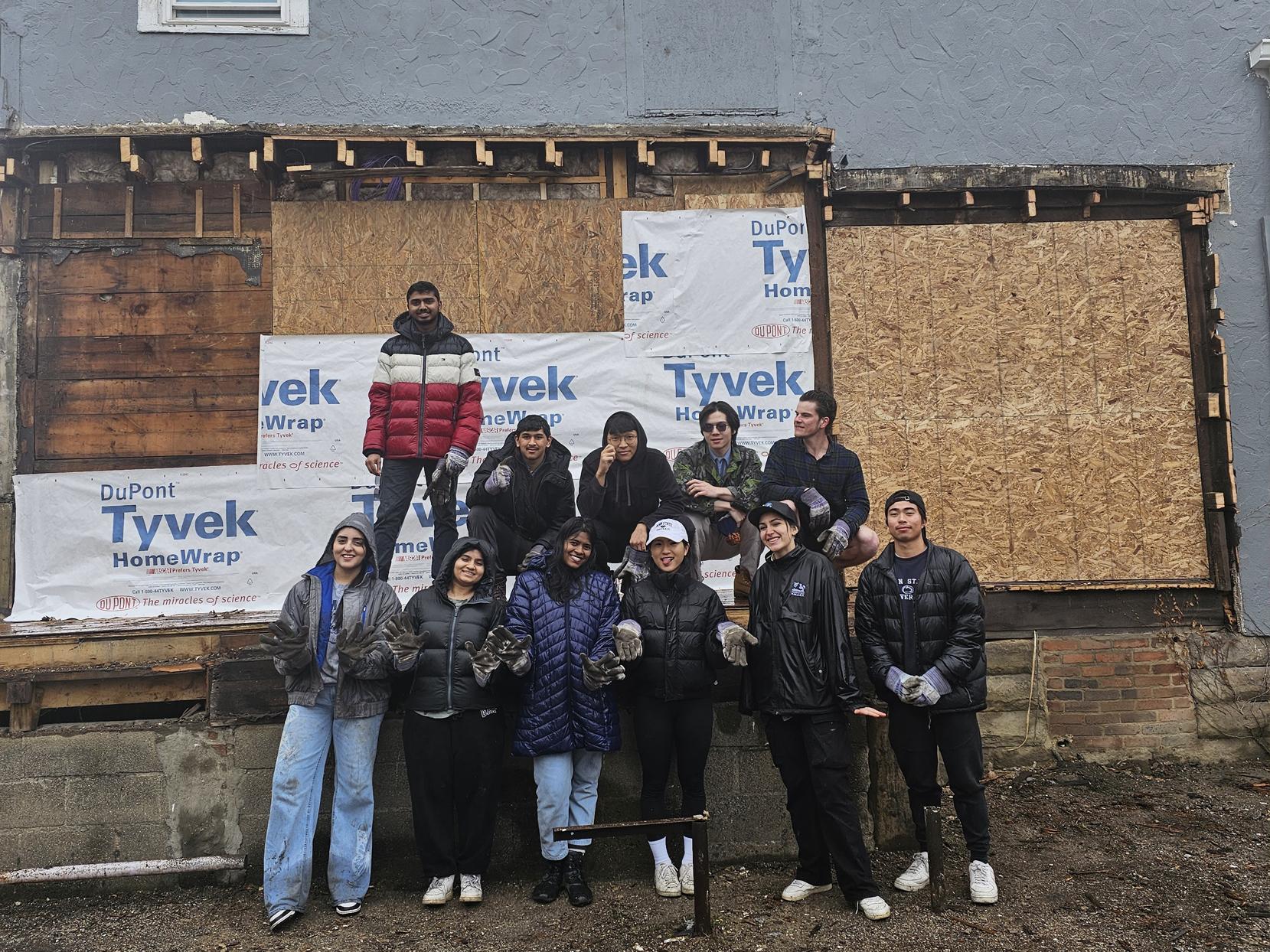 Students, some wearing dirty gloves, pose at a construction site