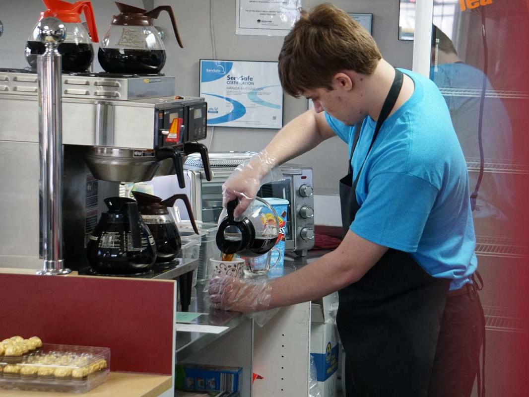 An employee pours a cup of coffee into a mug.