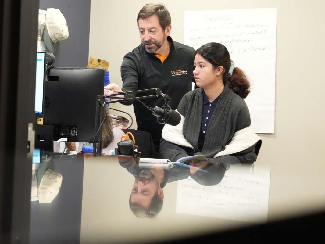 An instructor gesturing towards a computer screen next to a student seated at a desk.