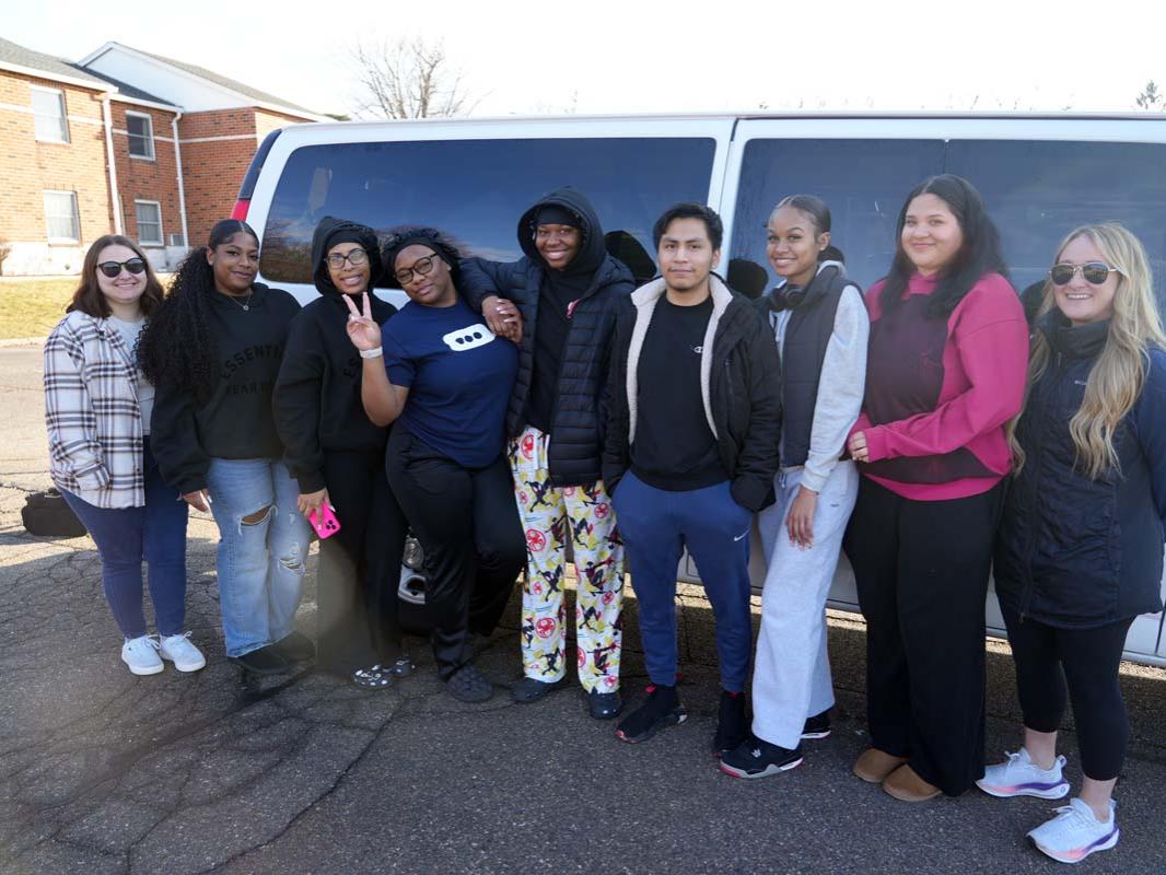 A group of students in a row lined up outside a white van in a parking lot.