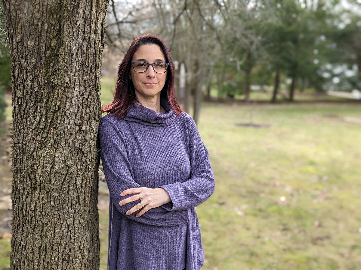 Liz Agler leaning against a tree wearing a purple dress