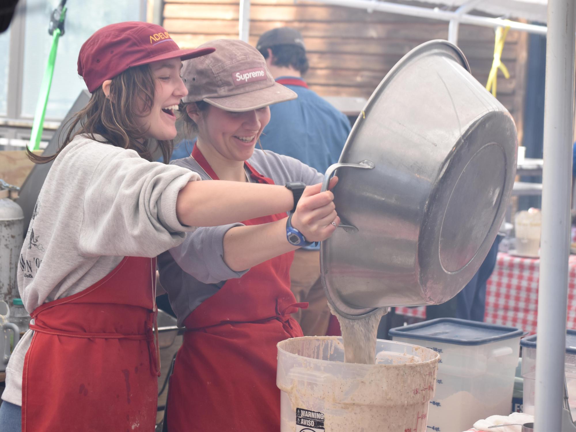Smiling volunteers pour pancake batter into bucket at outdoor festival