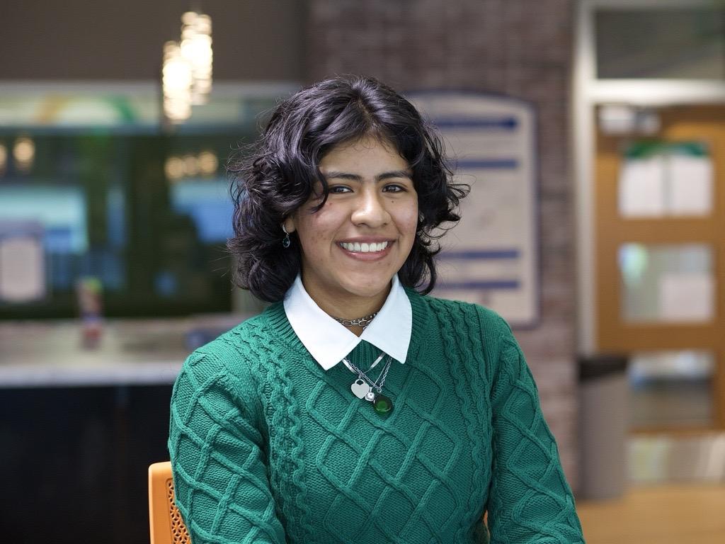 smiling dark-haired person wearing green sweater over white button-down