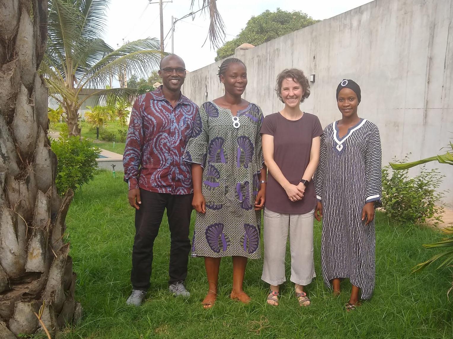 Four people standing in a line with a palm tree in the foreground