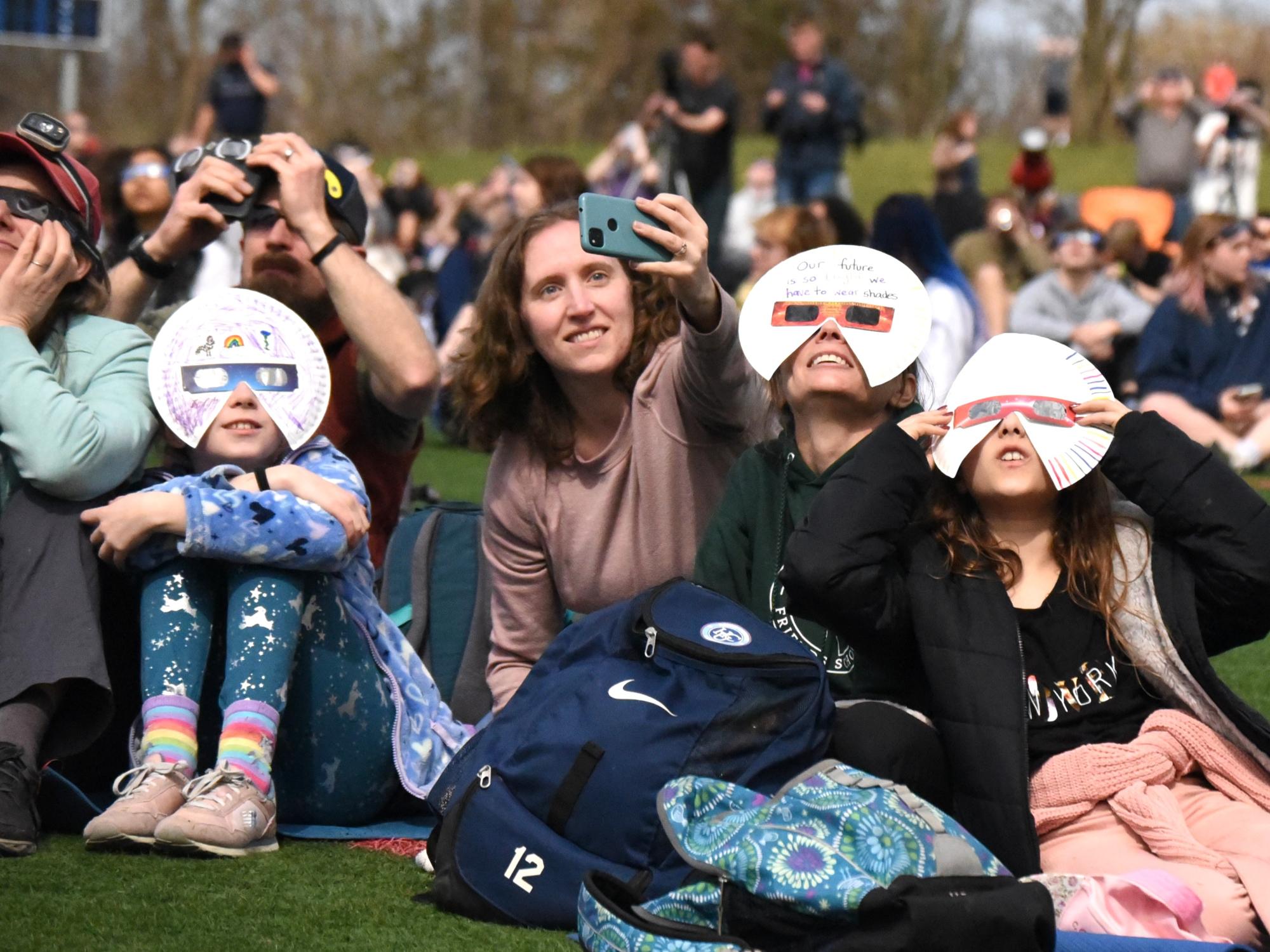 Crowd sitting on lawn stares up at eclipse