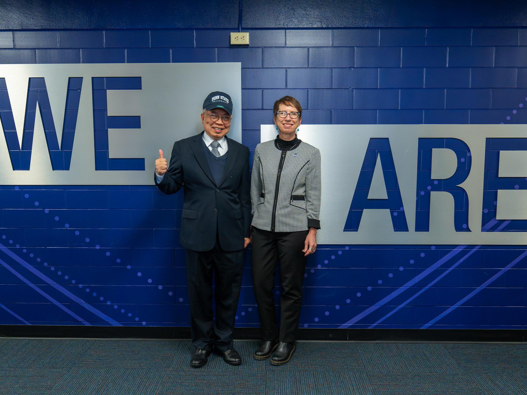 A man and a woman posing in front of a wall that says "We Are"