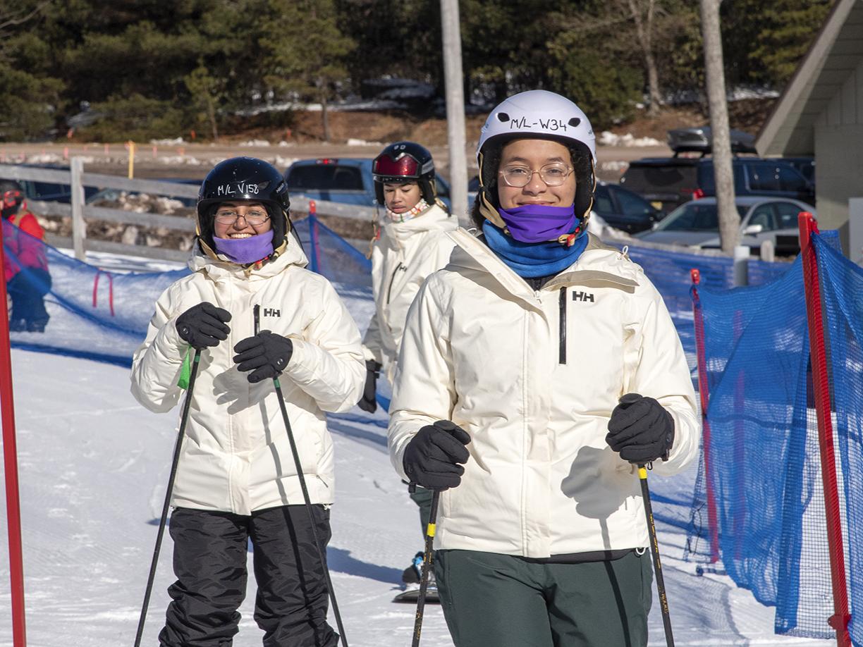 Students in white winter jackets skiing down a snow slope.