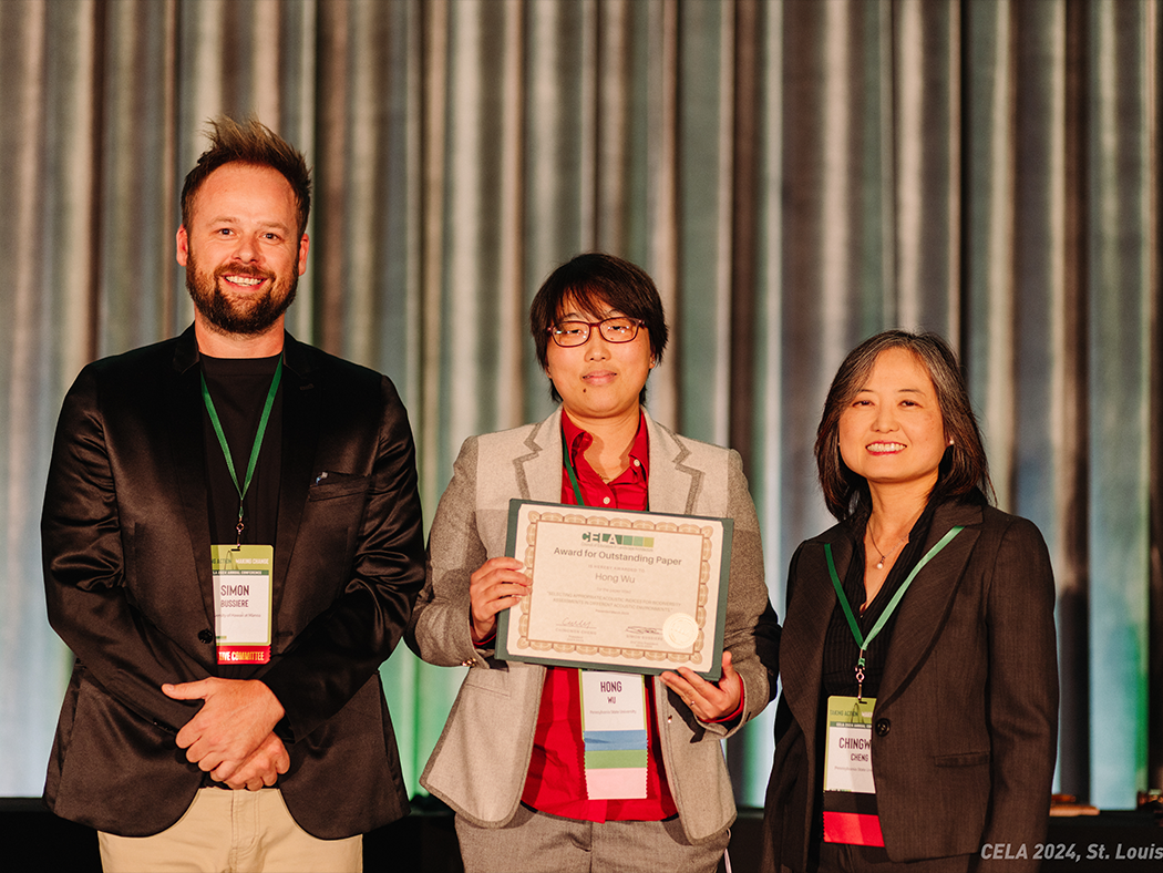 Hong Wu holding a certificate, at center, with a man to her left and a woman to her right.