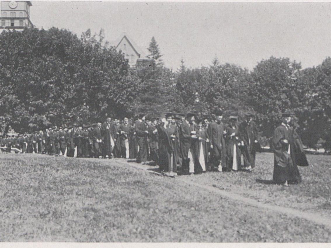 A group of students in caps and gowns walk in a line outdoors