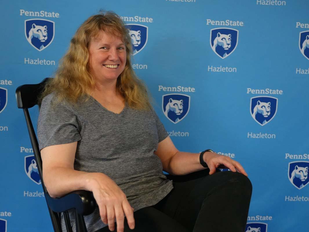 Blonde woman resting in rocking chair in front of light blue backdrop.