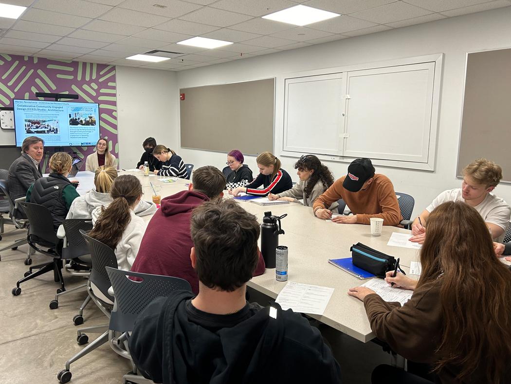 Graphic design students sit around a large table with their professor and a representative from Penn State Extension.