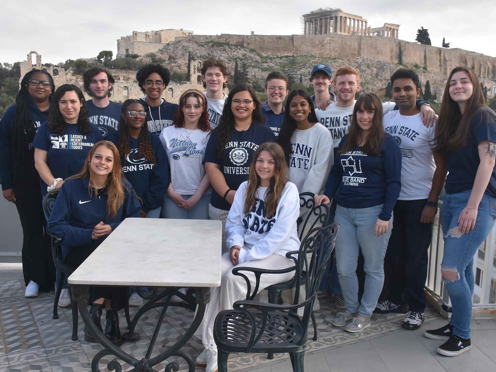 A group of students in Penn State apparel site and stand with the Acropolis in the background in Athens, Greece.