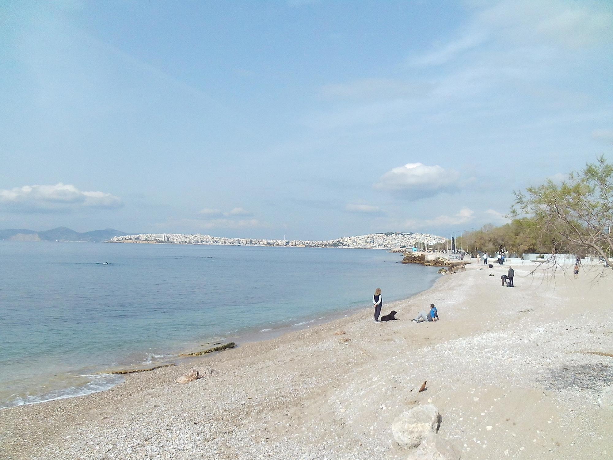 A few people stand and sit on the beach at Moschato, Greece.