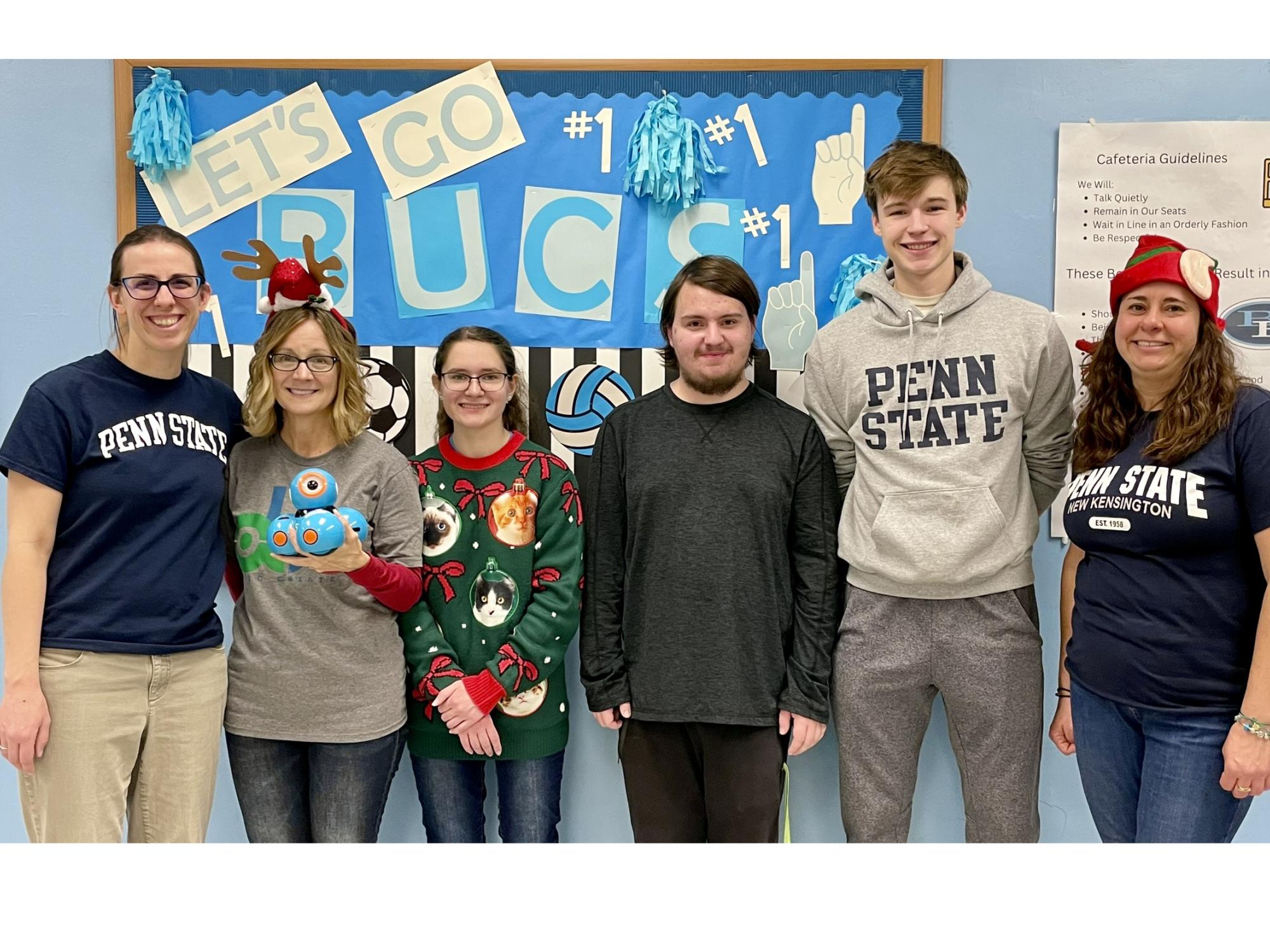 Students and faculty members stand in front of bulletin board for photo