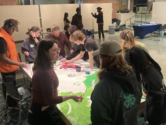 College-aged students gather around a large canvas to paint a mural
