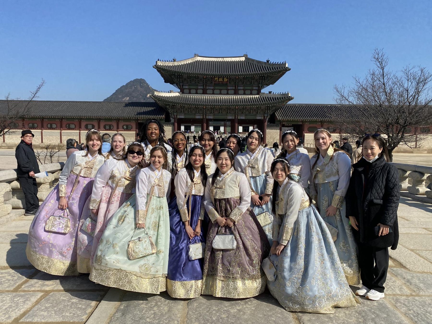 Students dressed in hanbok pose for a group picture in front of Gyeongbokgung Palace.