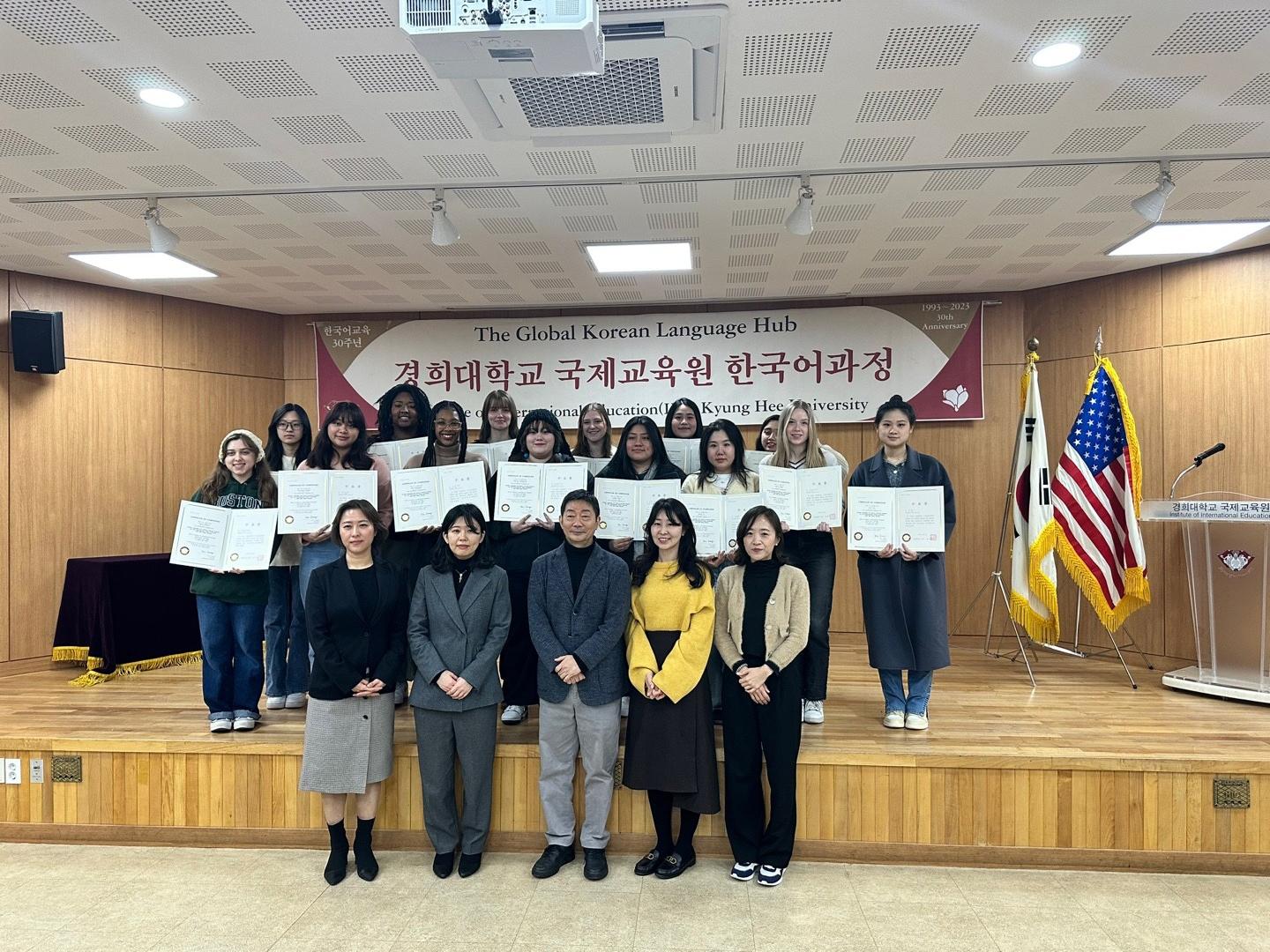 KOR 497 students pose with their course trip completion certifications on a small stage. 