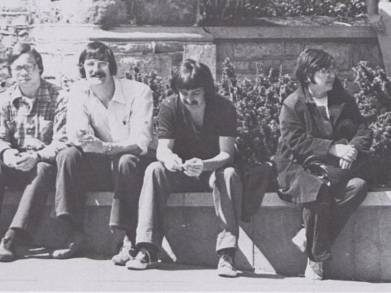 A group of students sit in front of a stone wall