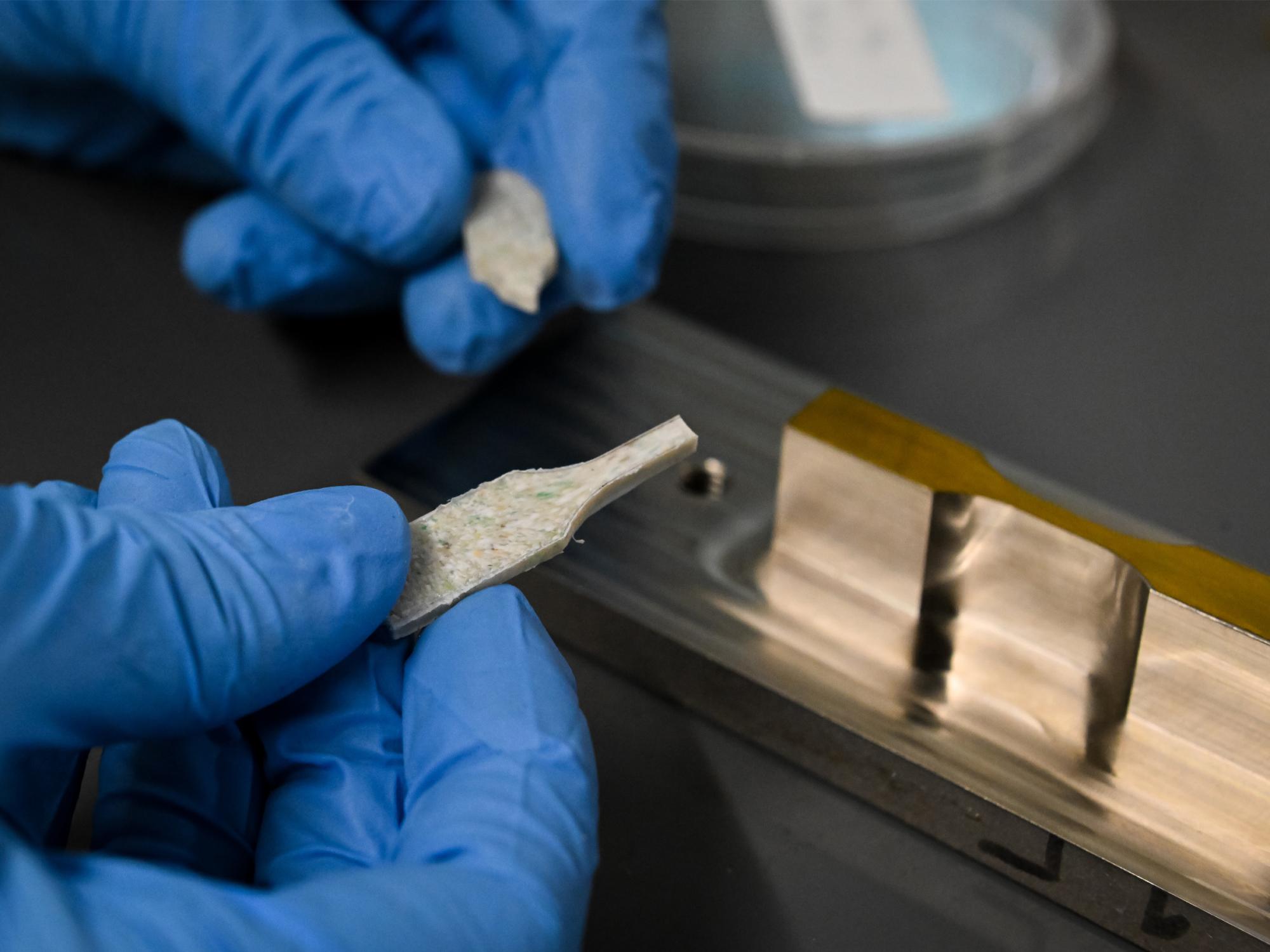 Gloved hands handle a composite sample of mixed plastics and ceramics.