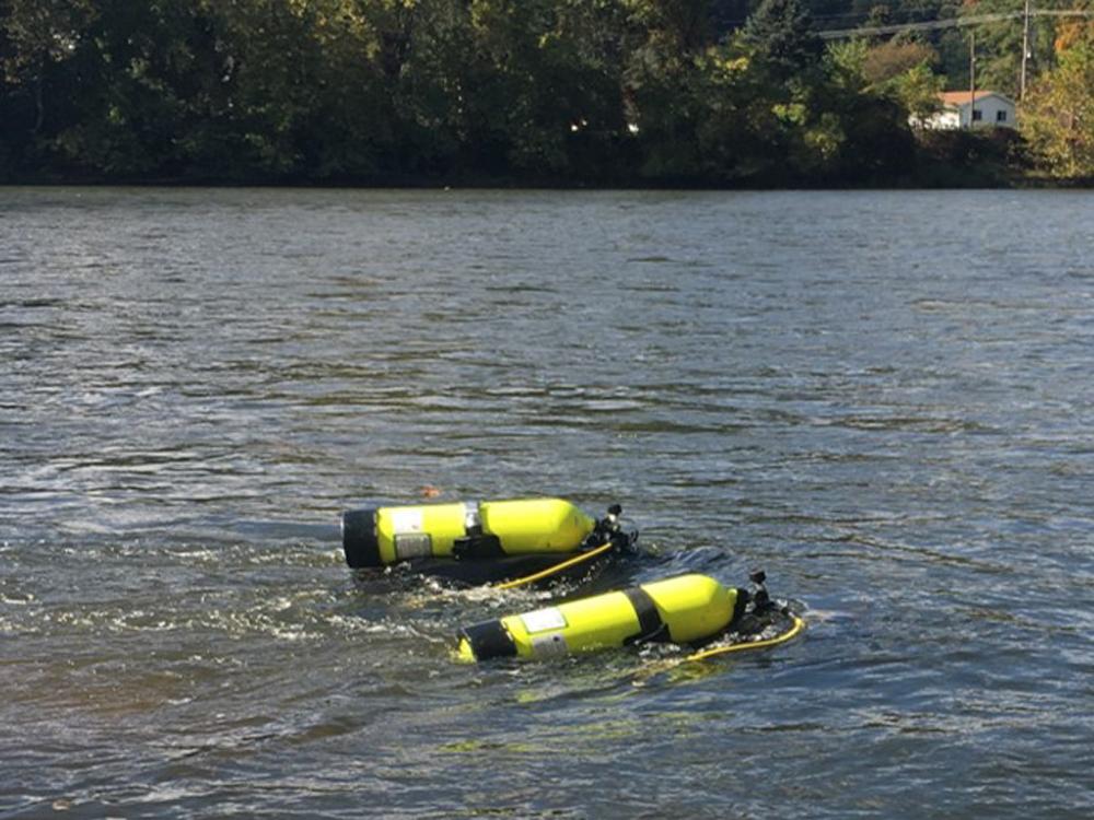 Two swimmers using scuba gear swim at the surface of a river.