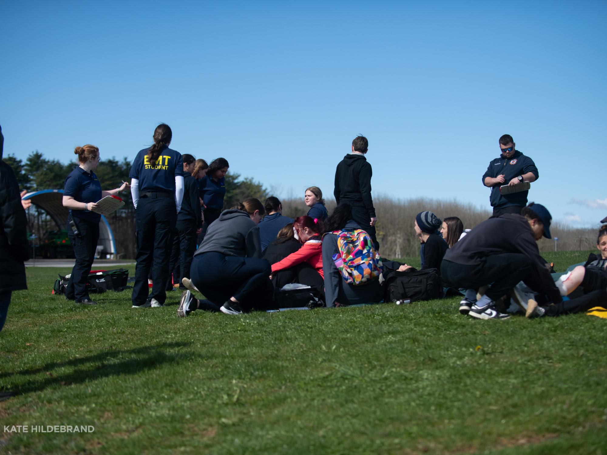 A group of students and Campus EMS staff work together to assess students faking injuries on a grassy field.