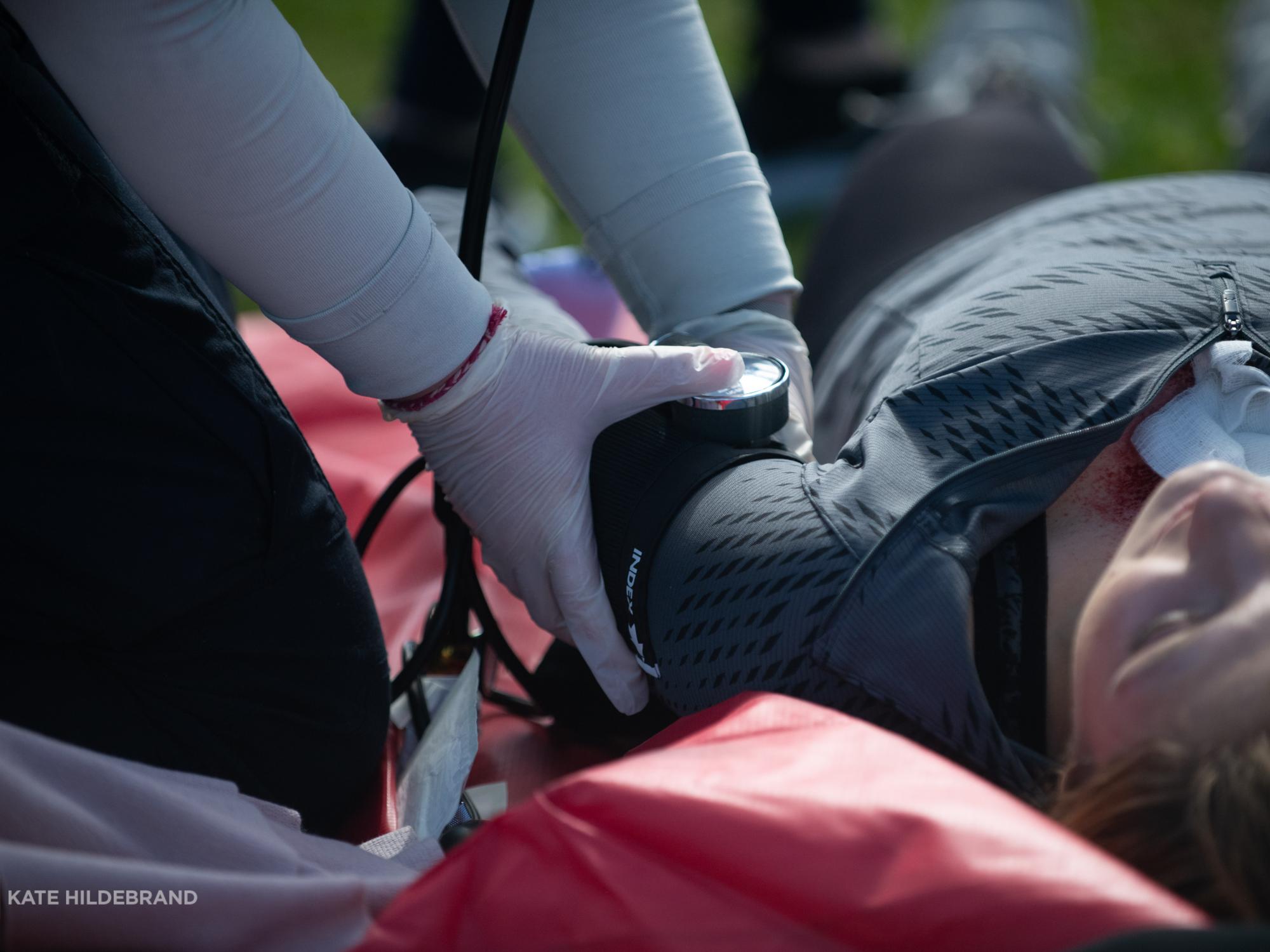 An athletic training student uses a blood pressure cuff to take the blood pressure of a student lying on the ground.